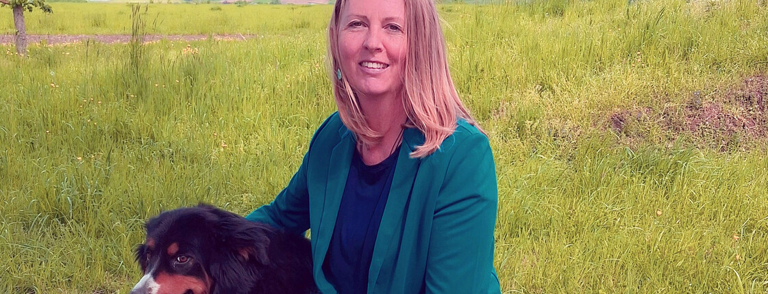 Eine Frau kniet mit einem Hund in einer Wiese.