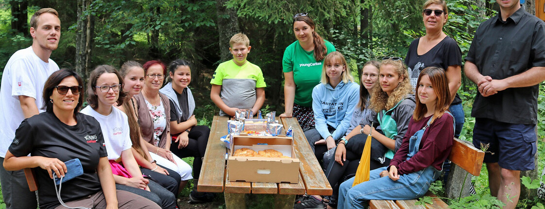 Grenztreffen youngCaritas Ein Gruppenfoto. Jugendliche sitzen im Wald ein einen Tisch.