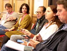 Fünf Personen sitzen auf Sesseln und hören den Vortragenden zu.