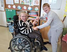 Ein Mädchen im Rollstuhl hält die Hände von einem lächelnden Mädchen