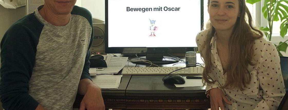 Ein Mann und eine Frau sitzen an einem Tisch. Zwischen ihnen steht ein Computer.
