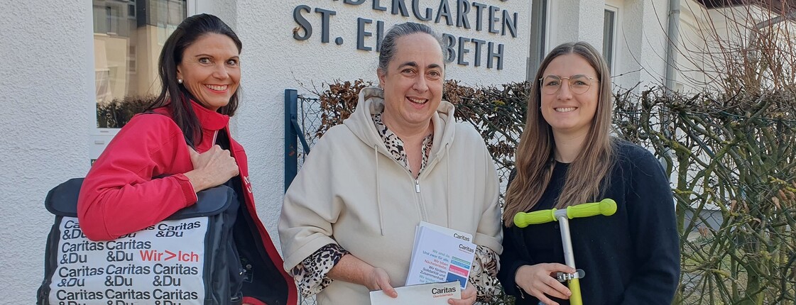 Drei Frauen stehen vor einem Kindergartengebäude und lächeln in die Kamera.