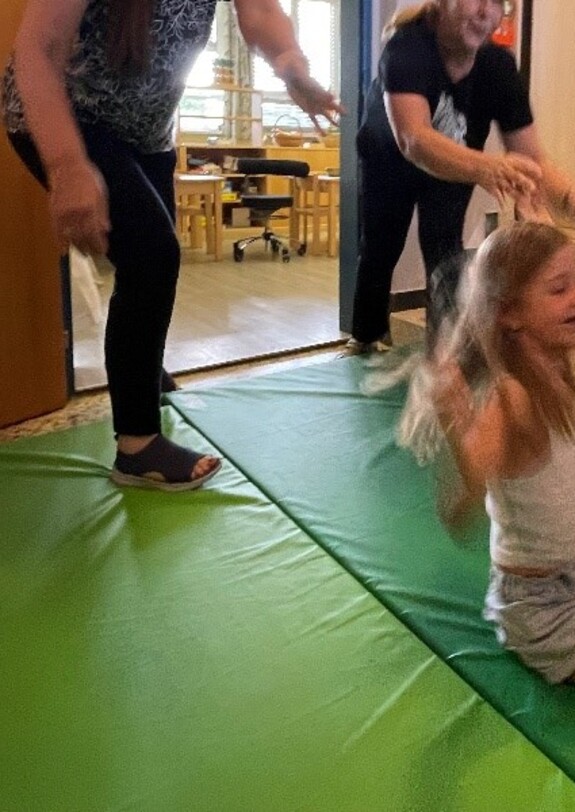 Zwei Erwachsene"werfen" ein Mädchen auf eine Matte.
