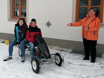 aritas-Familienhelferin im Freien mit zwei Kindern die auf einem Gokart sitzen.