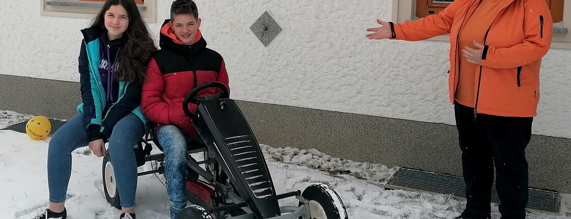 aritas-Familienhelferin im Freien mit zwei Kindern die auf einem Gokart sitzen.