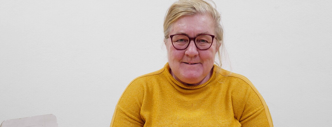 Frau in gelbem Pullover verpakct Kleinteile am Tisch.