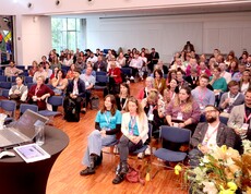 Ein Blick in einem vollgefüllten Saal, wo die Menschen auf Stühlen sitzen.