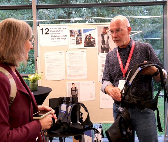 Ein Mann hält eine spezielle Weste in der Hand und erklärt einer Frau etwas darüber.