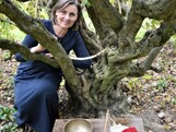 Frau mit halblangen Haaren hockt neben einem alten Baum.