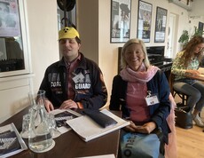 Ein Mann mit einer Blindenkappe und eine Frau sitzen an einem Tisch. 
