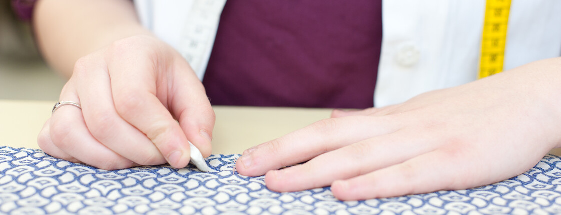 Zwei Hände markieren einen Stoff mit Nähkreide.