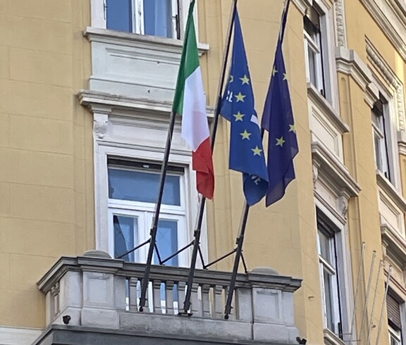 Eine Hauswand wo auf einem Balkon drei Flaggen wehen.