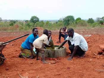 Eine Frau die gerade mit Männern und Kindern eine Biogasanlage mit Dung füllt lächelt.
