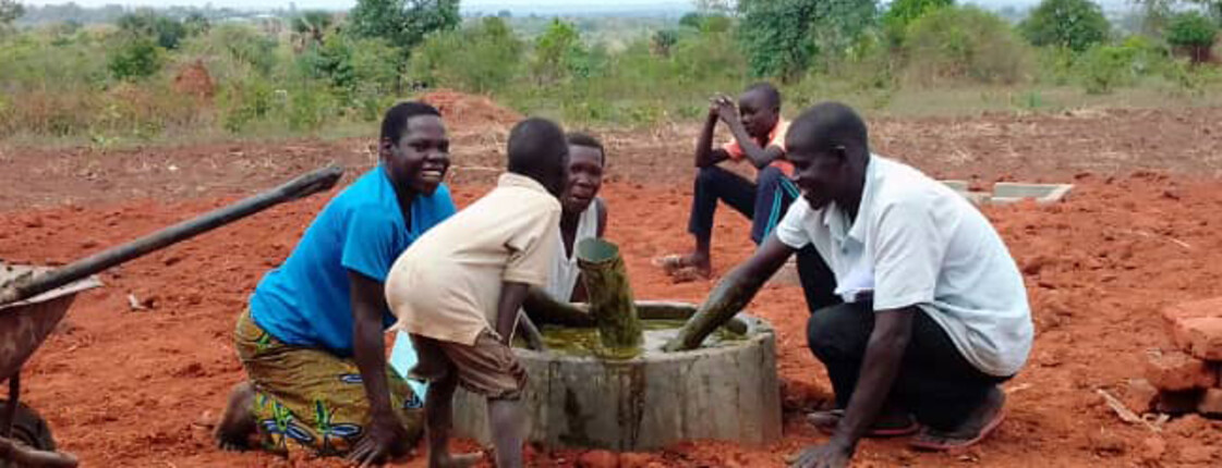 Eine Frau die gerade mit Männern und Kindern eine Biogasanlage mit Dung füllt lächelt.