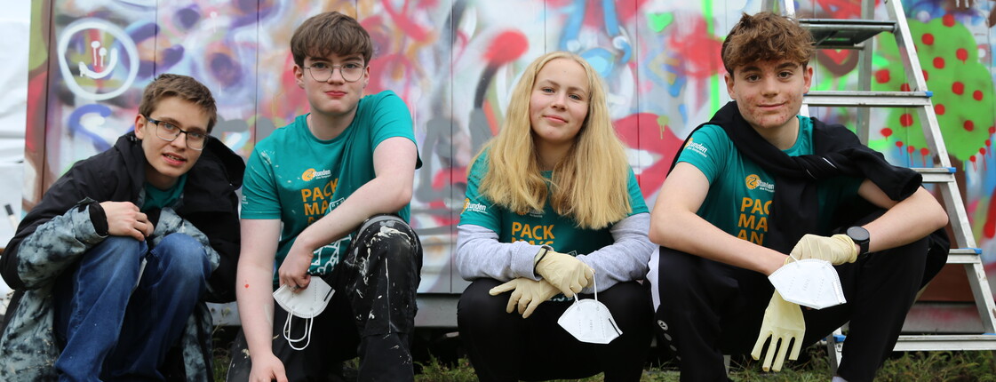 Vier Jugendliche hocken vor Spraydosen, dahinter ist eine Graffiti-Wand.