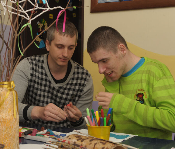 Ein Betreuer arbeitet mit einem Kind, das eine Beeinträchtigung hat, und hilft ihm bei einer kreativen Aktivität im Kinderdorf Gomel.
