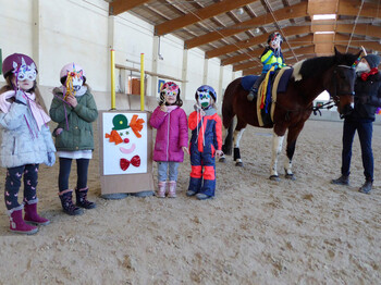 Kinder stehen in der Reithalle mit Einhornmasken und ein geschücktes Pferd steht daneben.