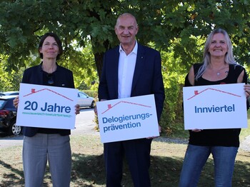 Zwei Frauen und ein Mann halten Schilder in der Hand, dahinter ein Baum