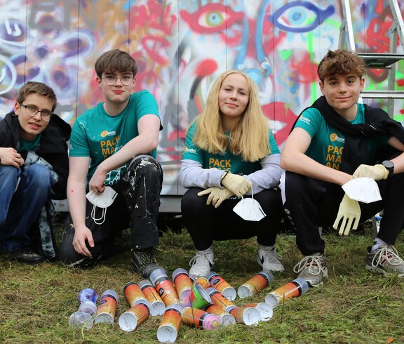 Vier Jugendliche in der Hocke vor einem Grafitti