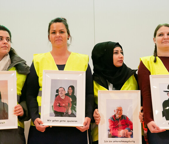 Vier Frauen halten jeweils ein Bild in der Hand. Auf den Bildern sind Personen abgebildet. 