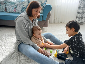 Eine Frau sitzt am Boden und spielt mit zwei Buben, die ebenefalls am Boden sitzten.