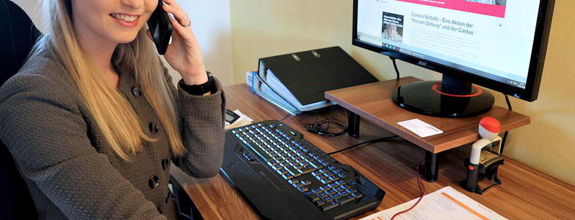 Eine Frau sitzt telefonierend am Arbeitsplatz vor dem Computer