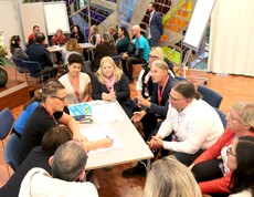 Blick von oben auf eine Gruppe von Personen die rund um einen Tisch sitzen und sich unterhalten.