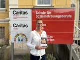 Eine Frau steht vor einer Werbetafel und hält ein Buch in den Händen.