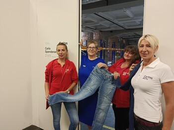 Vier Frauen stehen vor einer Tür die in eine Lagerhalle führt und halten eine Jeans in der Hand.