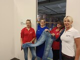 Vier Frauen stehen vor einer Tür die in eine Lagerhalle führt und halten eine Jeans in der Hand.