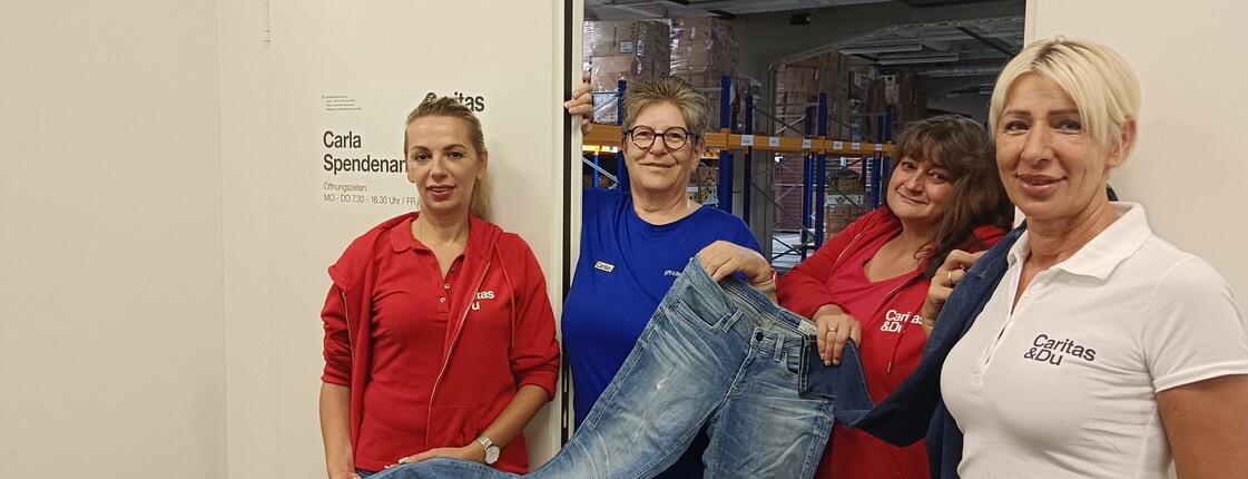 Vier Frauen stehen vor einer Tür die in eine Lagerhalle führt und halten eine Jeans in der Hand.