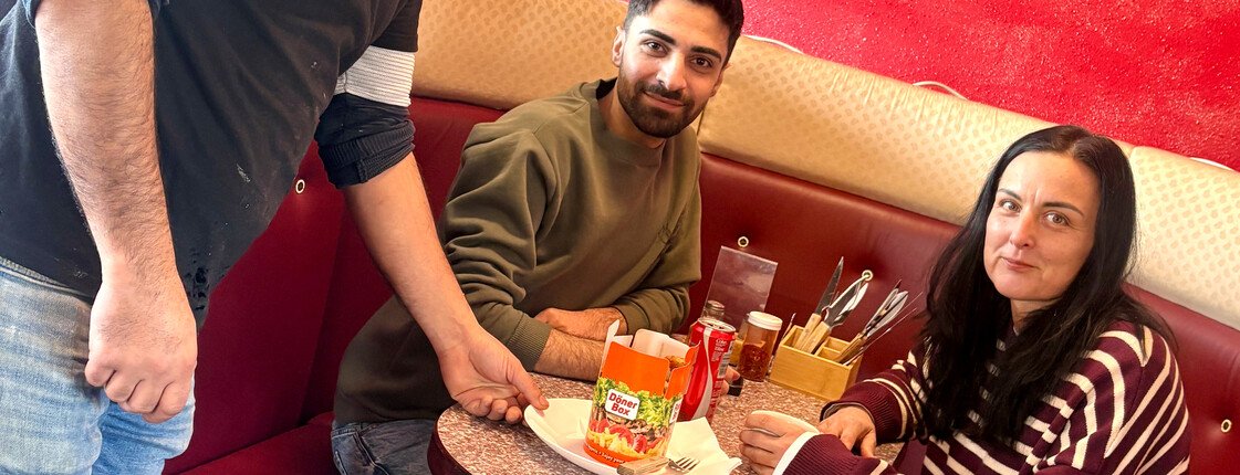 Eine Frau und ein Mann bekommen von einem Kellner einen Kebap serviert.