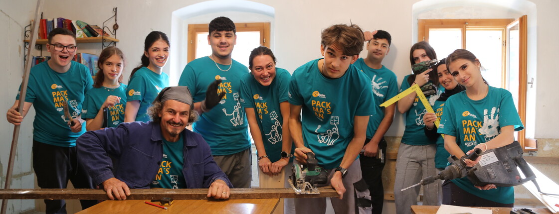 ein Mann sitzt am Tisch und eine Gruppe Jugendlicher steht hinter ihm