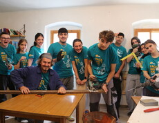 ein Mann sitzt am Tisch und eine Gruppe Jugendlicher steht hinter ihm