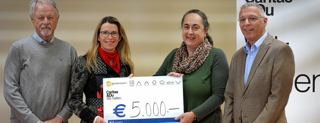 Vier Menschen, zwei Frauen und zwei Männer, stehen beisammen mit einem Spendencheck in Höhe von 5.000 Euro