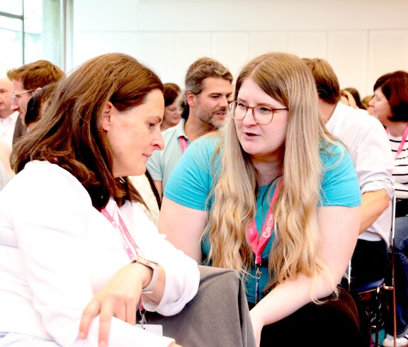 Zwei Frauen sitzen im Saal und unterhalten sich.