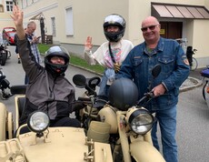 Eine Person sitzt im Beiwagen, zwei stehen neben dem Oldtimer-Motorrad am Caritas-Standort Engelhartszell