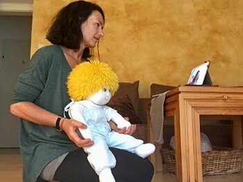 Eine Frau sitzt am Boden vor einem Tablet am Tisch und hält eine Handpuppe.
