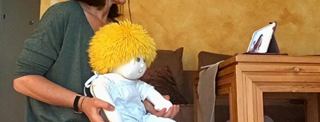 Eine Frau sitzt am Boden vor einem Tablet am Tisch und hält eine Handpuppe.