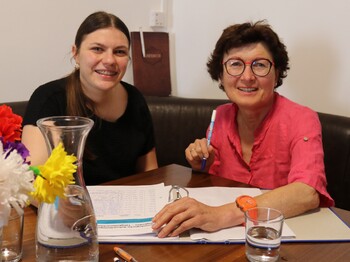 Eine junge und eine ältere Frau sitzen zusammen am Tisch.
