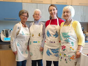 Drei ältere Damen und eine junge Frau stehen mit umgebundenen Kochschürzen in der Küche.