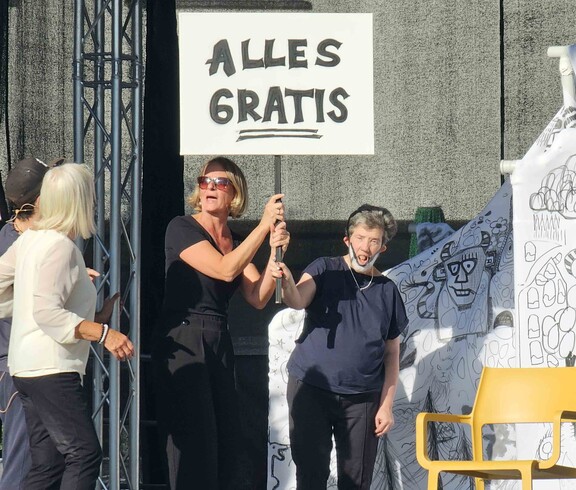 Menschen mit einem Schild "alles gratis" vor einem weiß-schwarzem Papierhaus