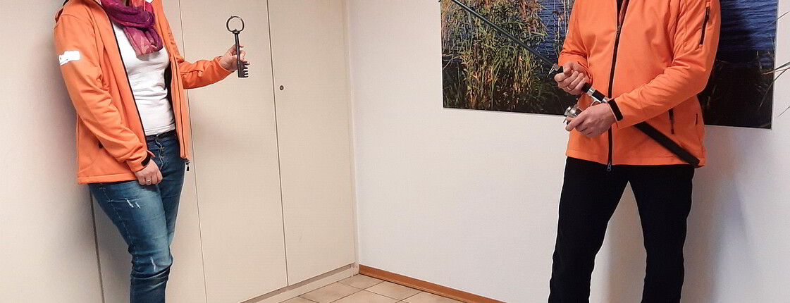 Schlüsselübergabe mittels einer Angel im Innenraum von einem Herrn zu einer Frau.