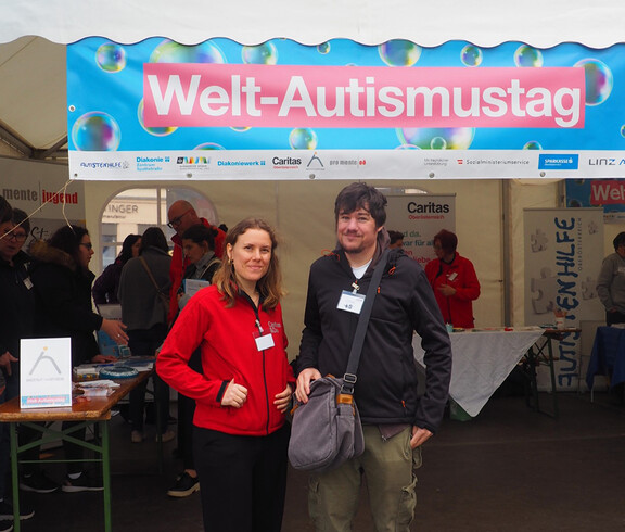 Zwei Personen stehen vor einem Pagodenzelt vor einem Banner. 