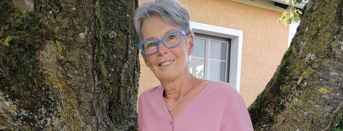 Eine Frau steht im Freien an einen Baum gelehnt und lächelt.