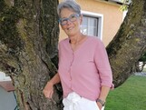 Eine Frau steht im Freien an einen Baum gelehnt und lächelt.