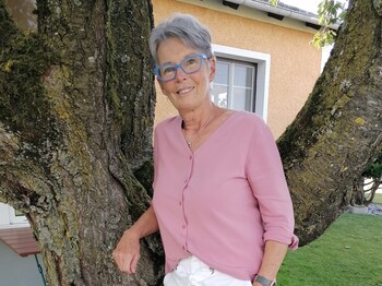 Ingrid Seilinger durfte schon viele bewegende Erfahrungen machen. Eine Frau steht im Freien an einen Baum gelehnt und lächelt.