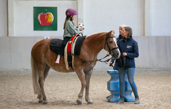 Ein Kind sitzt auf einem Pferd und hat einen Ball in einer Hand.