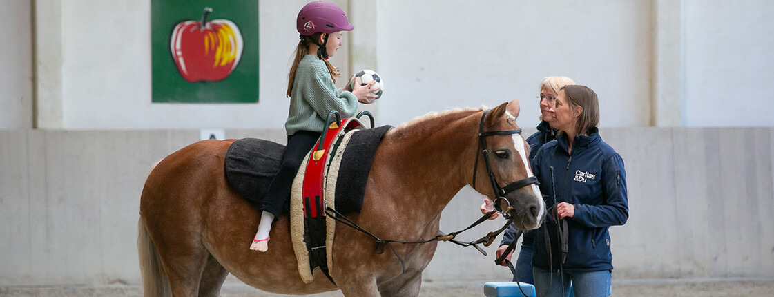 Ein Kind sitzt auf einem Pferd und hat einen Ball in einer Hand.
