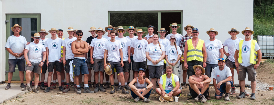 Gruppenfoto von ca. 30 Personen vor dem Rohbau eines Hauses.